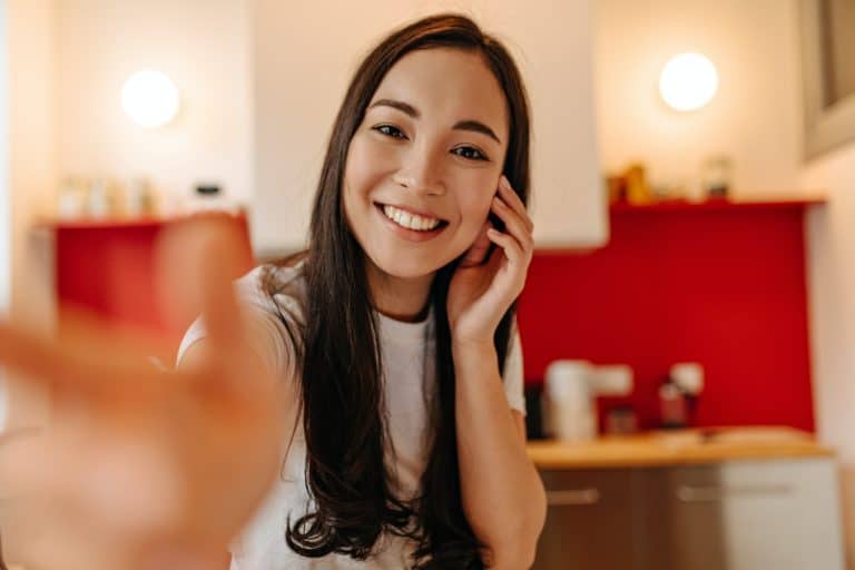 Brown-eyed lady in great mood posing in kitchen, smiling and taking selfie